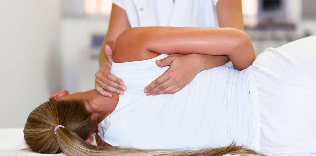 fisioterapeuta aplicando presion sobre el hombro de una paciente